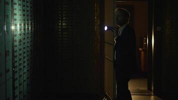 Man in suit spies Investigating vault safe holding a flashlight in dark room video