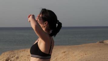 skön kvinna håller på med yoga på marin strand. ett vuxen flicka på ljus naturskön hav. modern roman av hav badning och Fantastisk sommar himmel på solnedgång. video