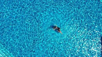 aéreo parte superior ver de Pareja teniendo divertido en el piscina, hombre es nadando y giros un niña en el agua. alegre Pareja disfrutando piscina a spa hotel juntos. zumbido vista, disfrutando verano vacaciones, fin de semana video