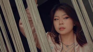 Young Asian woman peeking through blinds with a curious expression. video