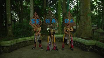 Traditional Indonesian dancers in colorful costumes performing in a lush green forest setting, with ornate wooden carvings video