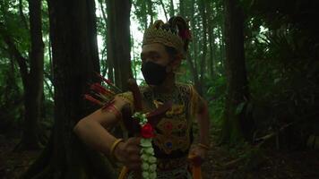 Person in traditional attire with a mask and holding arrows, standing in a lush green forest video