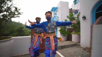 Two joyful dancers in colorful outfits and face masks performing a traditional dance on a street video