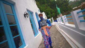 Blurred motion of a person wearing a mask and colorful attire walking by a traditional white and blue building video