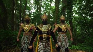 Three women in traditional ethnic costumes and face masks standing in a lush green forest, showcasing cultural attire video