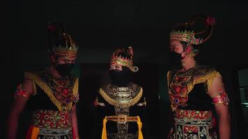 tre interpreti nel tradizionale balinese costumi e maschere, in piedi nel un' debolmente illuminato camera video