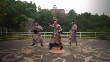 Three performers in traditional Asian attire and masks dancing outdoors with greenery and a building in the background video