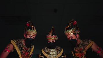 Three performers in traditional Javanese dance costumes with elaborate headdresses, captured in a dramatic stage lighting setting video