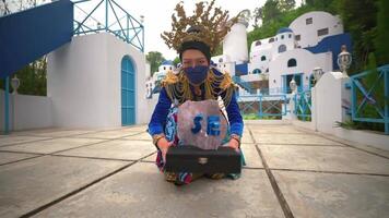 Person in colorful attire holding a tablet in front of a picturesque white and blue building, reminiscent of Mediterranean architecture video