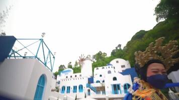 A person in vibrant traditional clothing and a mask performs a dance with blue ribbons, set against a whimsical backdrop video