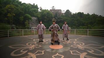 Three performers in traditional Japanese masks and kimonos dancing on an outdoor stage with greenery in the background, showcasing cultural heritage video