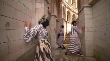 Three individuals in quirky outfits and masks playfully posing on a spiral staircase, creating a sense of motion and fun video