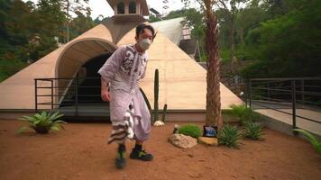 Rear view of a person walking towards a modern, dome-shaped building surrounded by lush greenery, wearing a backpack and a patterned outfit video