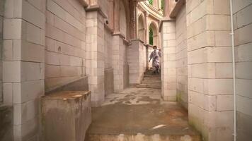 A man in a casual suit running through an old, narrow corridor with stone walls, arches, and steps video