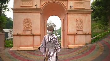 Person in elaborate traditional mask and costume with intricate designs, standing in front of a historic building with ornate architectural details video