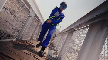 Stylish person in blue jumpsuit posing confidently on an urban rooftop with industrial backdrop. video