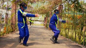 Two people in blue overalls and safety goggles playfully dancing in a garden with a vine-covered archway. video