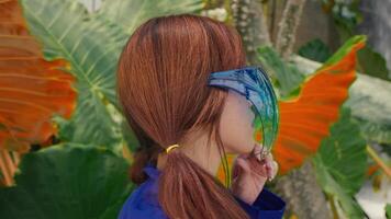 achterzijde visie van een vrouw met een blauw masker in een tropisch instelling, omringd door weelderig groen. video