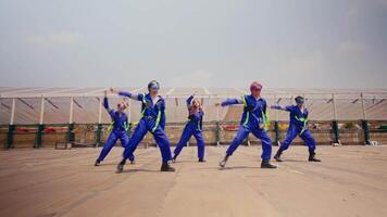 Group of workers in blue uniforms and hard hats performing synchronized exercises at an industrial site. video