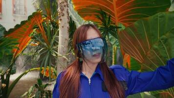 Female worker in safety gear standing in a tropical greenhouse with lush foliage. video