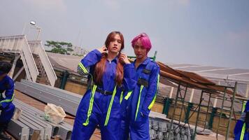 Two young adults with colorful hair in blue work wear against an industrial backdrop. video