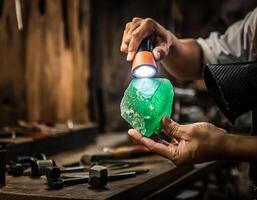 A craftsman hand holds a chunk of raw green jade and uses a flashlight to examine photo