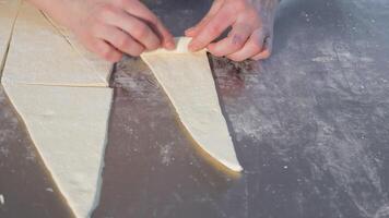 vrouw handen twist een stuk van deeg in een driehoek naar maken een stokbrood. detailopname van vrouw handen draaien bagels. video