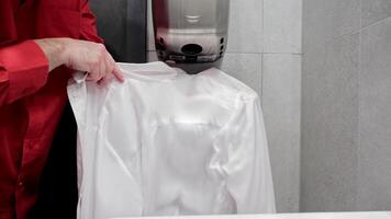 Man drying white shirt under hand dryer in public restroom, A close-up image showing a man wearing a red shirt, drying a white shirt under a hand dryer in a public restroom video