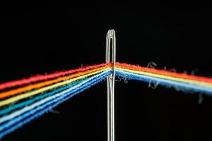 multi-colored threads for sewing in the form of a rainbow pass through an antique needle on a black background photo