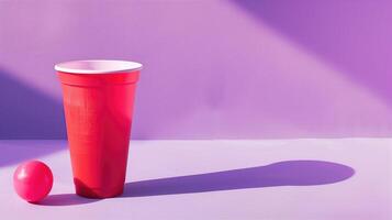 Red plastic cup with a white ping pong ball on a purple shaded background creating a playful mood photo