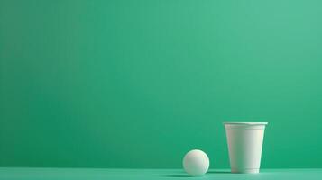 A single beer pong cup accompanied by a white ball against a green background, hinting at fun times ahead photo