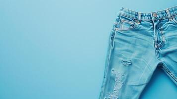 A trendy pair of light blue denim jeans with fashionable rips, laid flat on a matching blue background photo