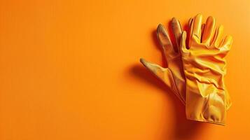 A pair of yellow rubber gloves laid flat on a vivid orange surface, casting soft shadows photo