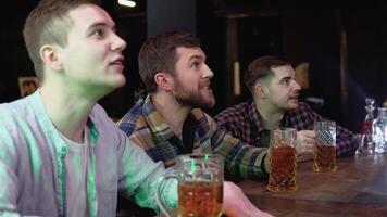 Group of friends watches TV in the sporstbar. Their team scores the goal and wins. Young people cheer video