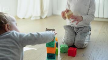 Two childs building tower of block toys sitting on floor in sunny bedroom video