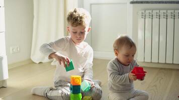 Two childs building tower of block toys sitting on floor in sunny bedroom video