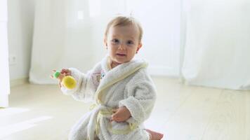 Kid girl in bathrobe playing with a doll at home or kindergarten. Cute child playing on the floor in nursery video