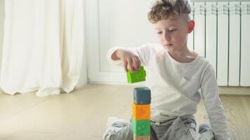 peu garçon bâtiment la tour de bloquer jouets séance sur sol dans ensoleillé chambre à coucher. éducatif Jeu pour bébé et tout-petit. les enfants construire jouet maison video