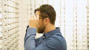 Portrait of a funny male client in several glasses near showcase with eyewear video