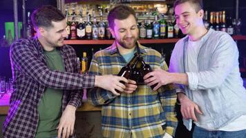 Handsome friends clinking bottles of beer and smiling while resting at the pub video