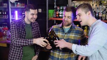 Handsome friends clinking bottles of beer and smiling while resting at the pub video