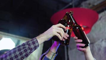 bonito amigos tilintar garrafas do Cerveja e sorridente enquanto em repouso às a bar video