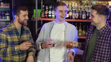 Three friends in a bar chatting and pouring whiskey from glasses video