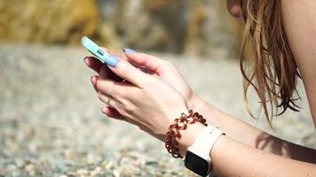 Woman with smartphone. Close-up of woman's hands holding vertical mobile phone and swiping up finger application page against background of sea and beach video