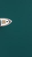 Aerial yacht on calm sea. Luxury cruise trip. View from above of white boat on deep blue water. Aerial top down view of rich yacht sailing sea. Summer journey on luxury ship. Vertical video