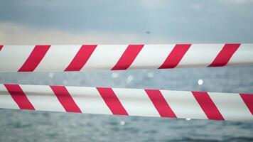 rood wit waarschuwing plakband barrière lint swinging in de wind aan de overkant exotisch zee strand achtergrond zonder mensen. Nee binnenkomst rood wit voorzichtigheid plakband. Nee vakantie concept, vertraagd reis, Nee zomer plannen video