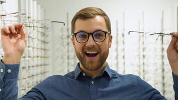 salud cuidado, vista y visión concepto - contento hombre elegir lentes a óptica Tienda video