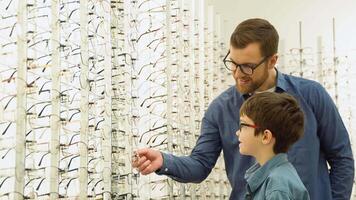 Family buy glasses. Father and son in a blue shirts choosing glasses video