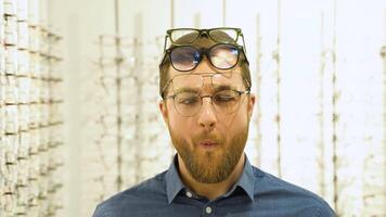 portrait de une marrant Masculin client dans nombreuses des lunettes près vitrine avec lunettes video