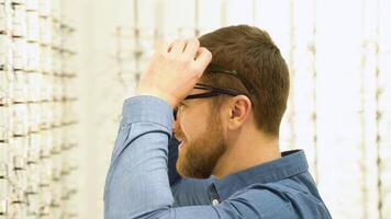 portrait de une marrant Masculin client dans nombreuses des lunettes près vitrine avec lunettes video